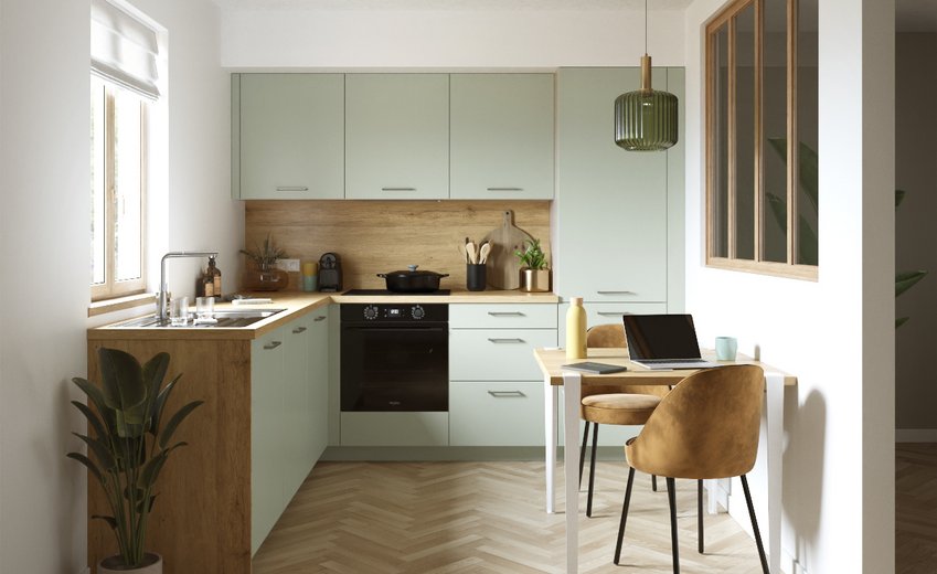 Cuisine moderne vert pastel et bois clair, disposition en L avec coin repas, sol parquet chevrons et suspension verte.